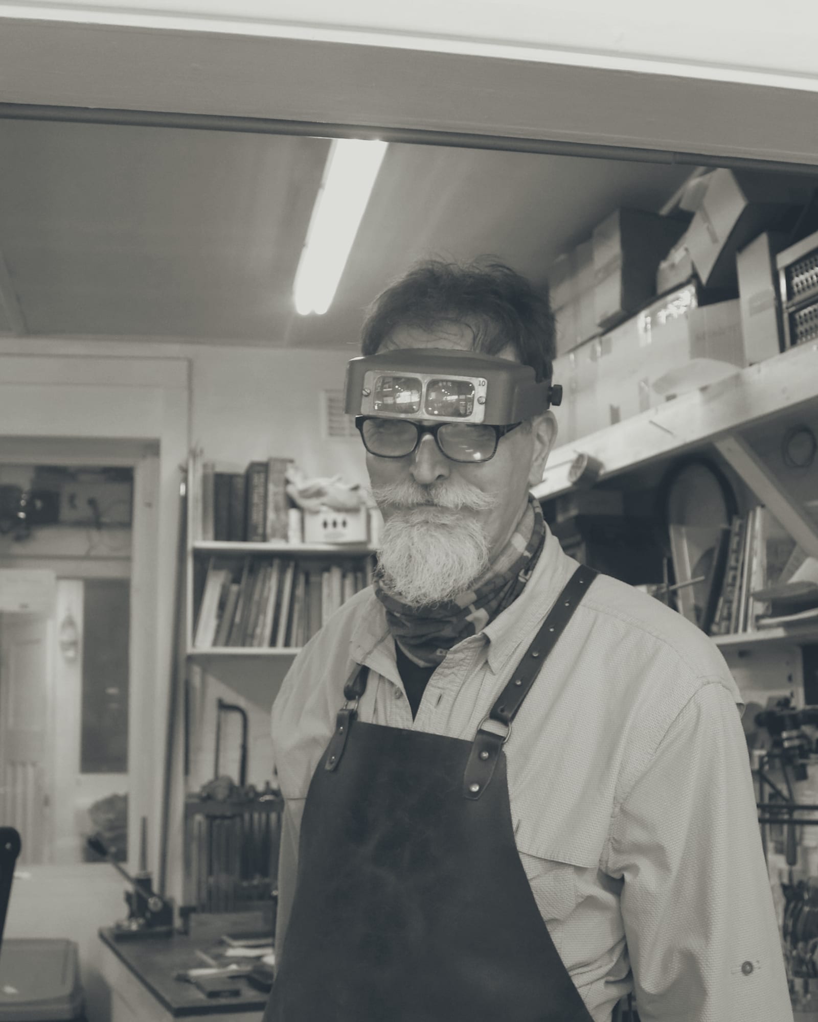 A jeweler in an optical visor, standing at the workshop bench